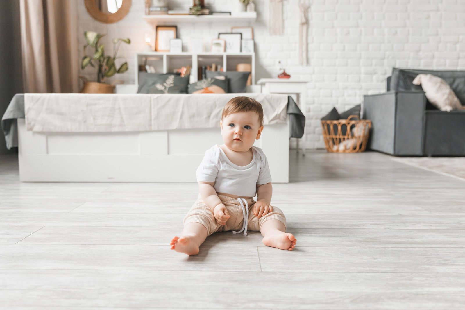 Portrait of a 7-9 month old baby in a home interior, on vinyl flooring. A curious, smiling child explores the world around him. A cute baby is sitting on the floor.
